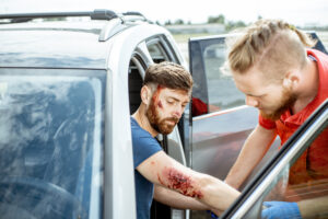 Ambulance worker examining injuries of a man sitting near the car after the road accident, providing emergency medical assistance